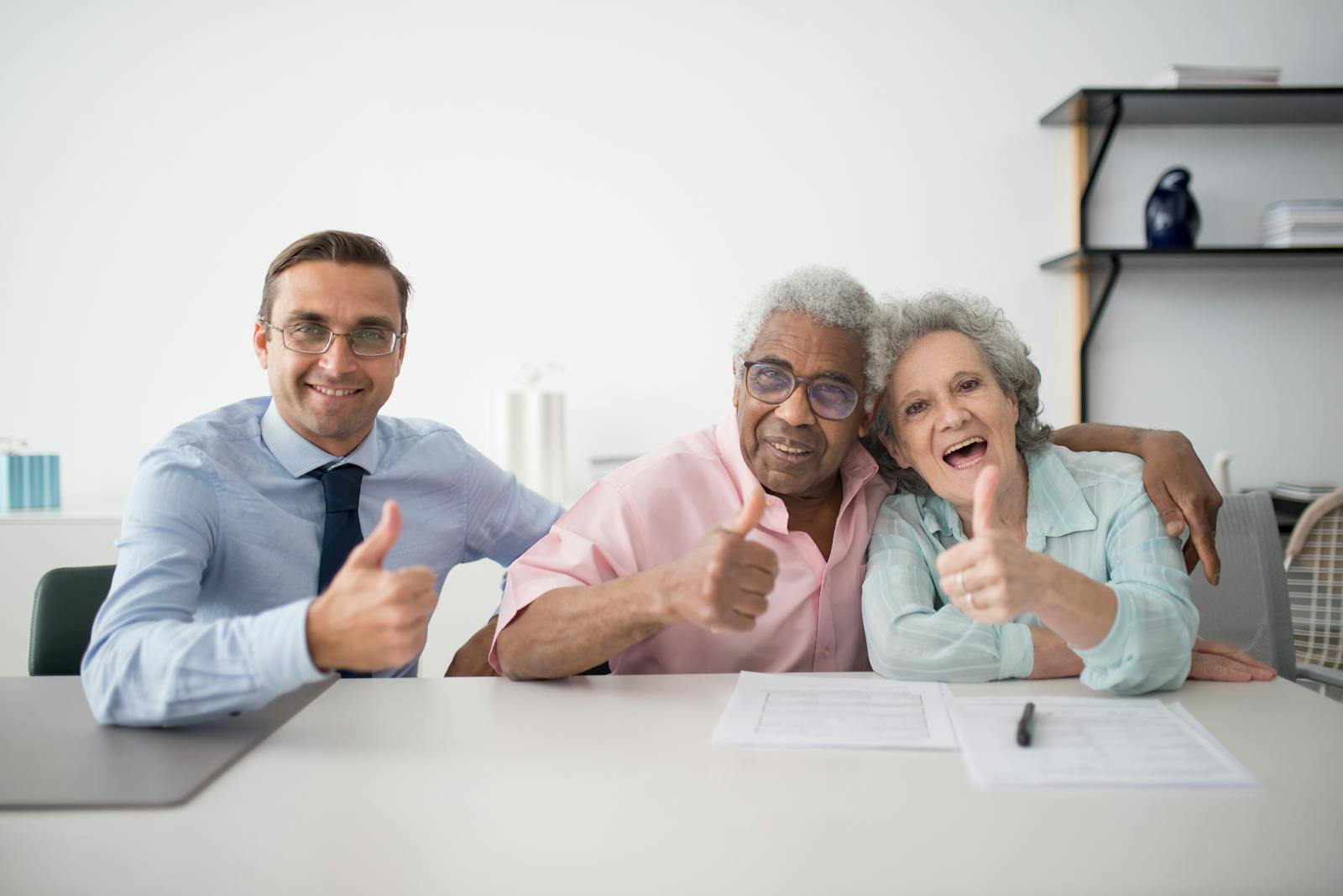 Elderly couple with consultant giving thumbs up in an office setting, showcasing positive interaction.
